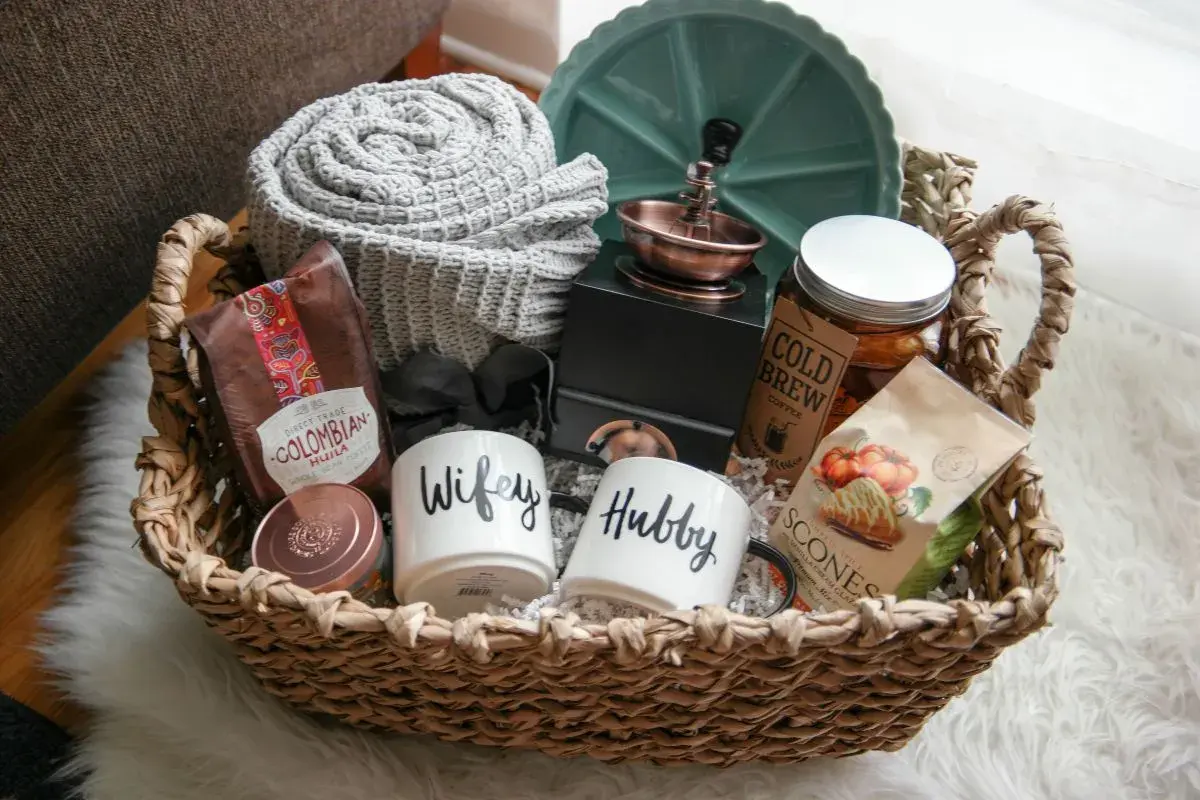 Cesta de mimbre con un kit para recién casados: tazas "Wifey" y "Hubby", café colombiano, scones, manta y más.