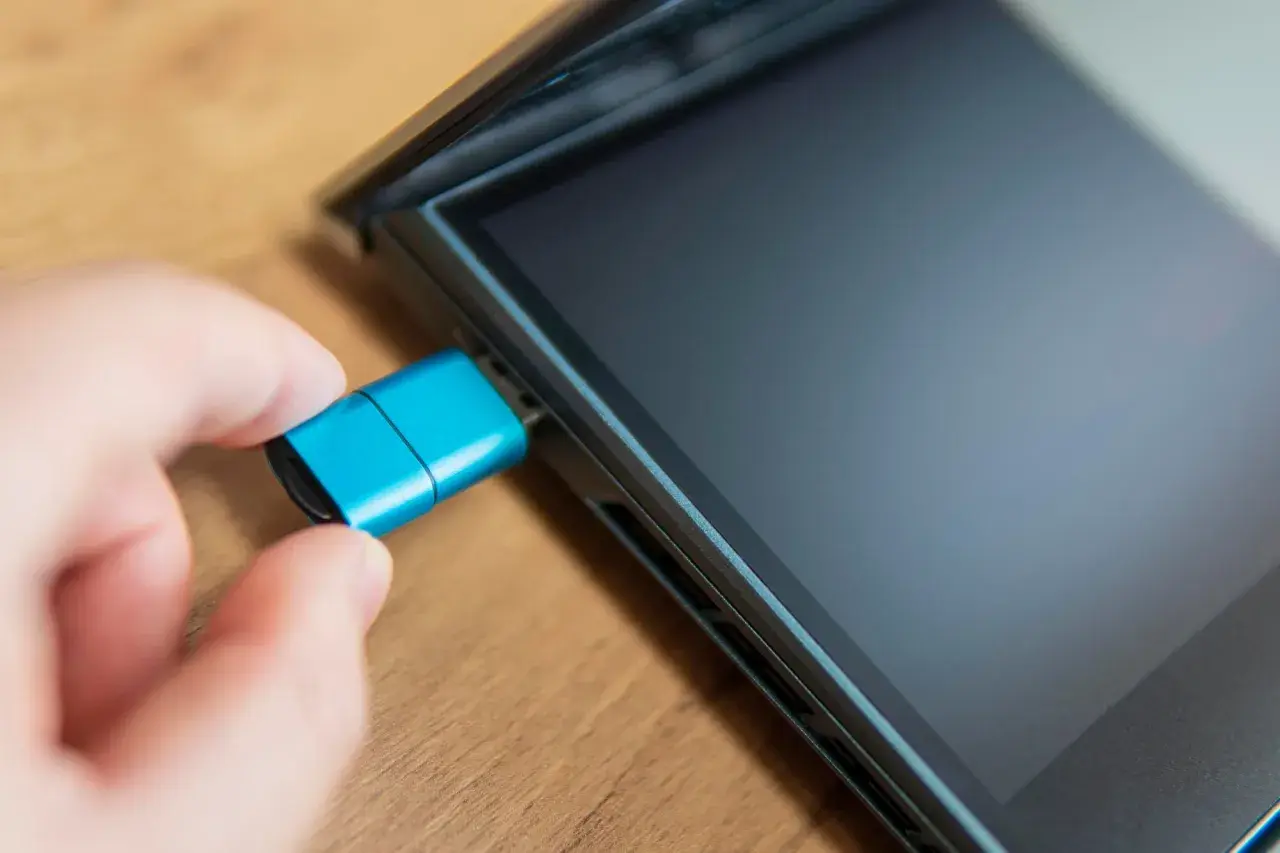 Dłoń podłącza niebieski pendrive do iPada. Dowiedz się, jak podłączyć pendrive do iPada, aby łatwo przenosić pliki.