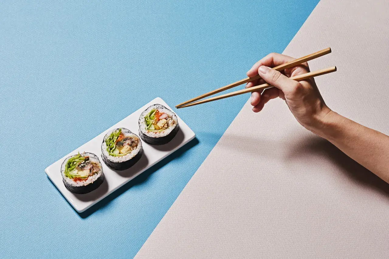 Dłoń z pałeczkami do sushi pokazuje, jak trzymać pałeczki do sushi, by złapać pyszne rolki.