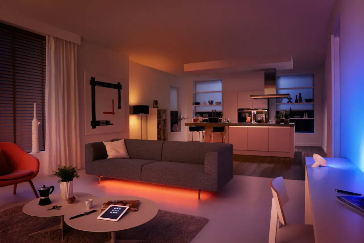 Sofá moderno con iluminación led ambiental. Cocina integrada, arte abstracto y silla naranja. Las led caracteristicas crean una atmósfera acogedora.