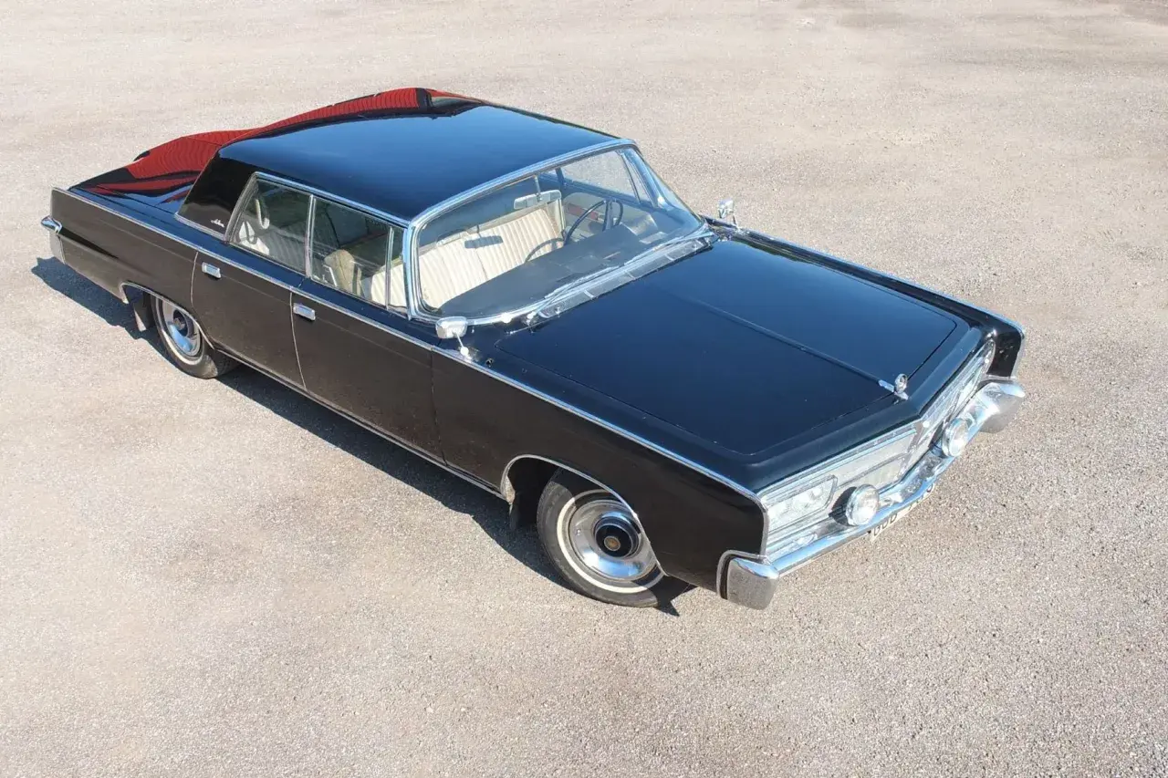 Svart imperial bil med kromdetaljer och ljus interiör, parkerad på grus. En klassiker som väcker beundran.