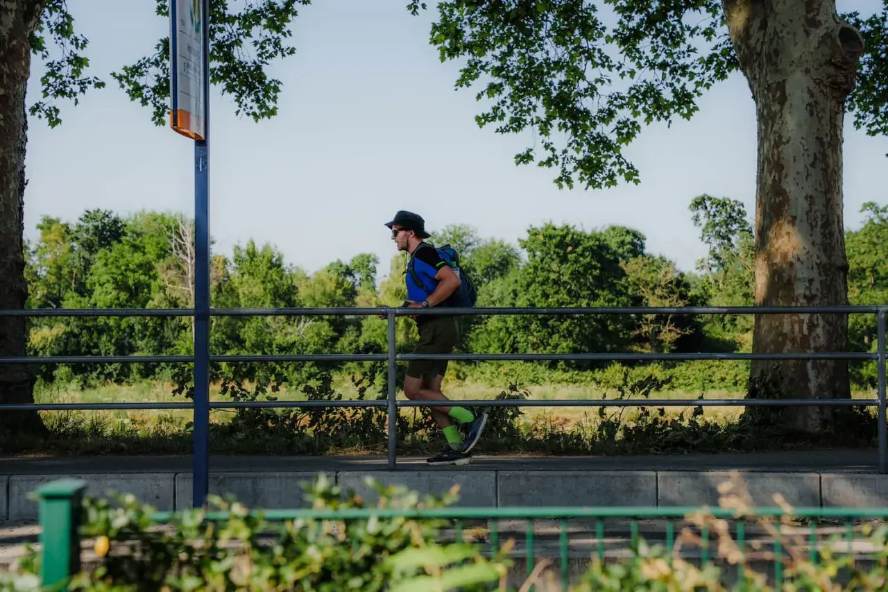 Mann mit Rucksack und Hut läuft auf einem Weg in Mannheim, umgeben von Bäumen und Grün.