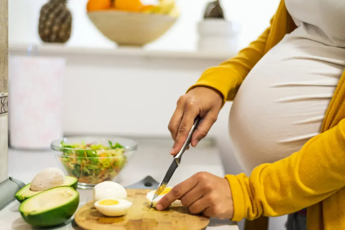 Schwangere bereitet gesunde Mahlzeit zu. Eier in der Schwangerschaft sind wichtig. Sie schneidet gekochtes Ei für Salat.