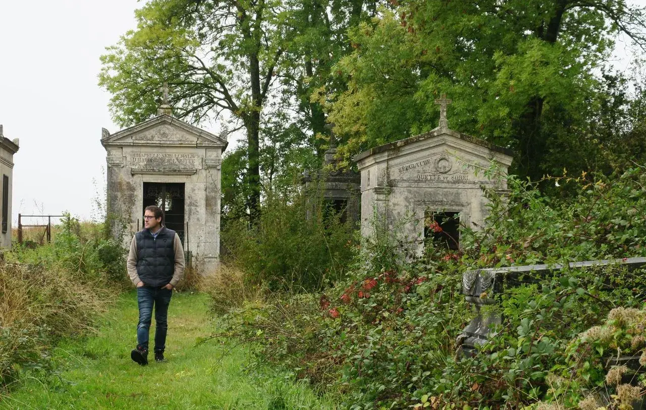 Un homme marche dans un cimetière abandonné en France, entouré de mausolées envahis par la végétation.
