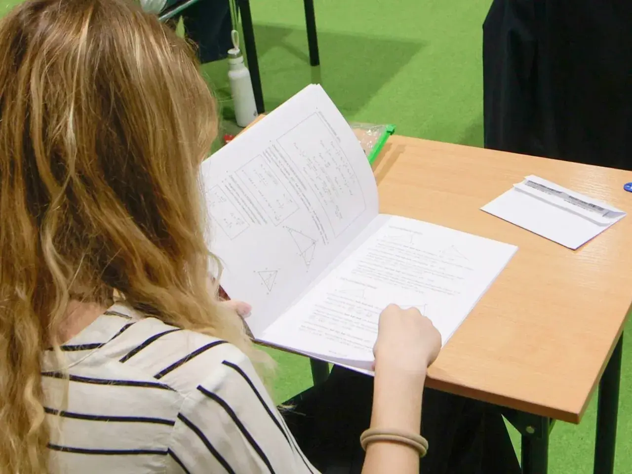 Dziewczyna z blond włosami czyta arkusz z zadaniami matematycznymi.