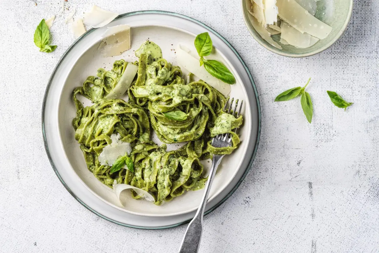 Un piatto di pasta al pesto, condita con una cremosa salsa verde, guarnita con scaglie di parmigiano e foglie di basilico fresco.
