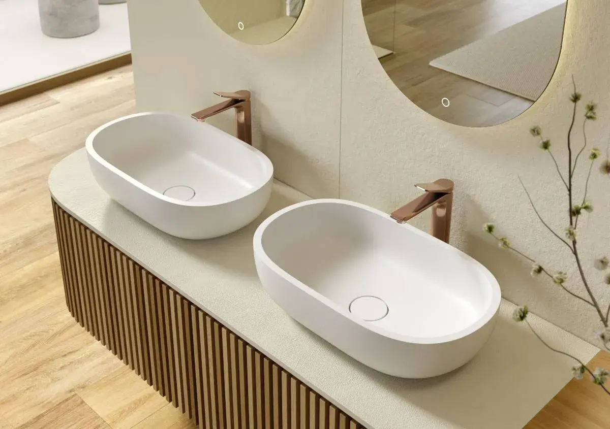 Due lavabi ovali bianchi su un mobile bagno su misura con finitura a listelli verticali. Rubinetteria color rame.