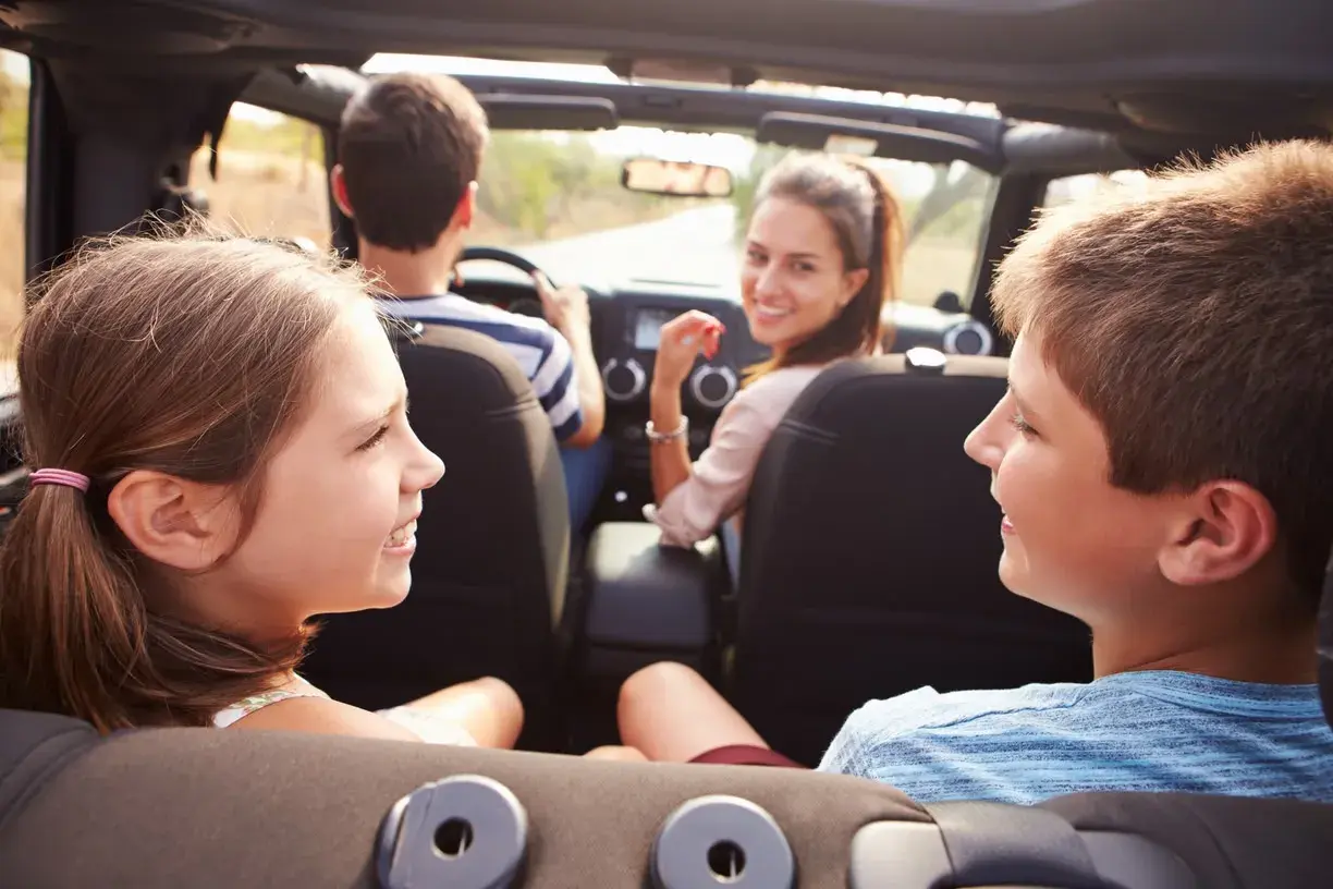 Famiglia in auto, divertiti con giochi da fare in macchina a voce. I bambini sorridono, la madre guarda indietro.
