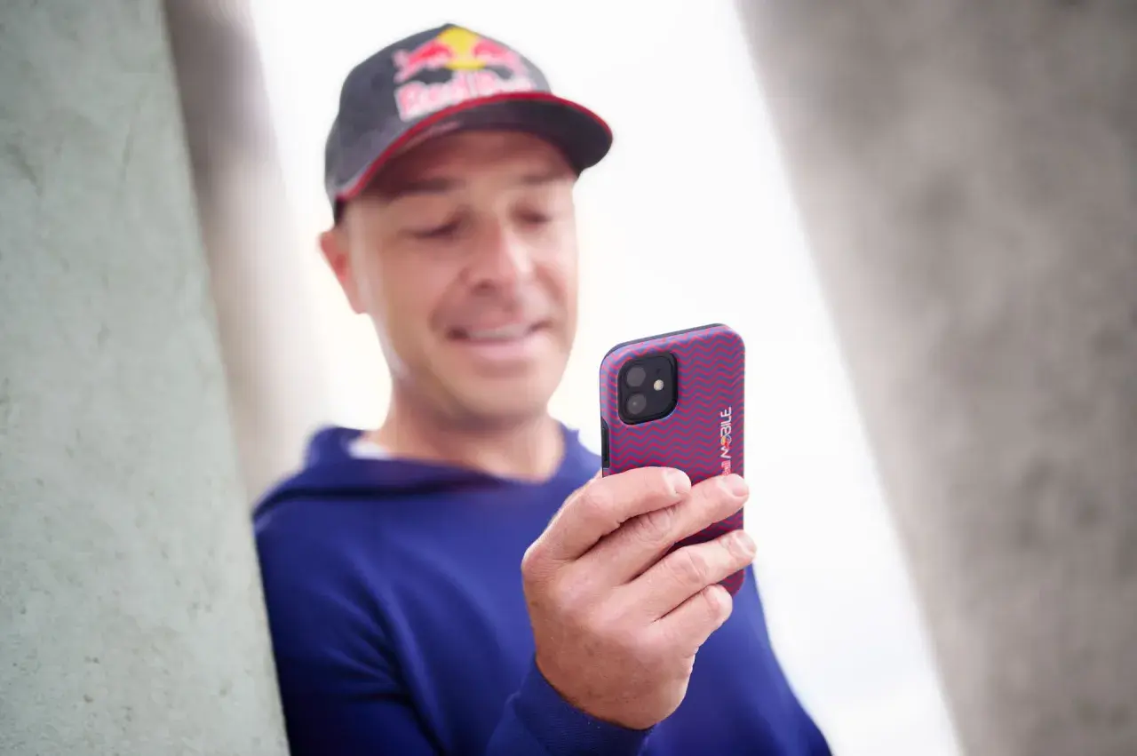 Mężczyzna w czapce Red Bull trzyma telefon z wzorzystym etui. Wzory na telefonie są czerwono-niebieskie.