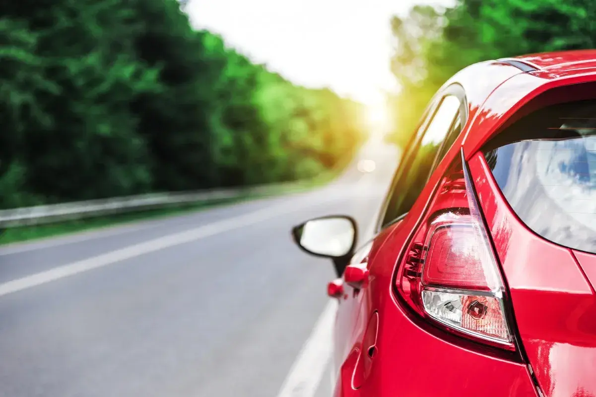 Auto rossa su strada panoramica, con sole che filtra tra gli alberi. Potrebbe indicare una **perdita potenza motore benzina** durante un viaggio.