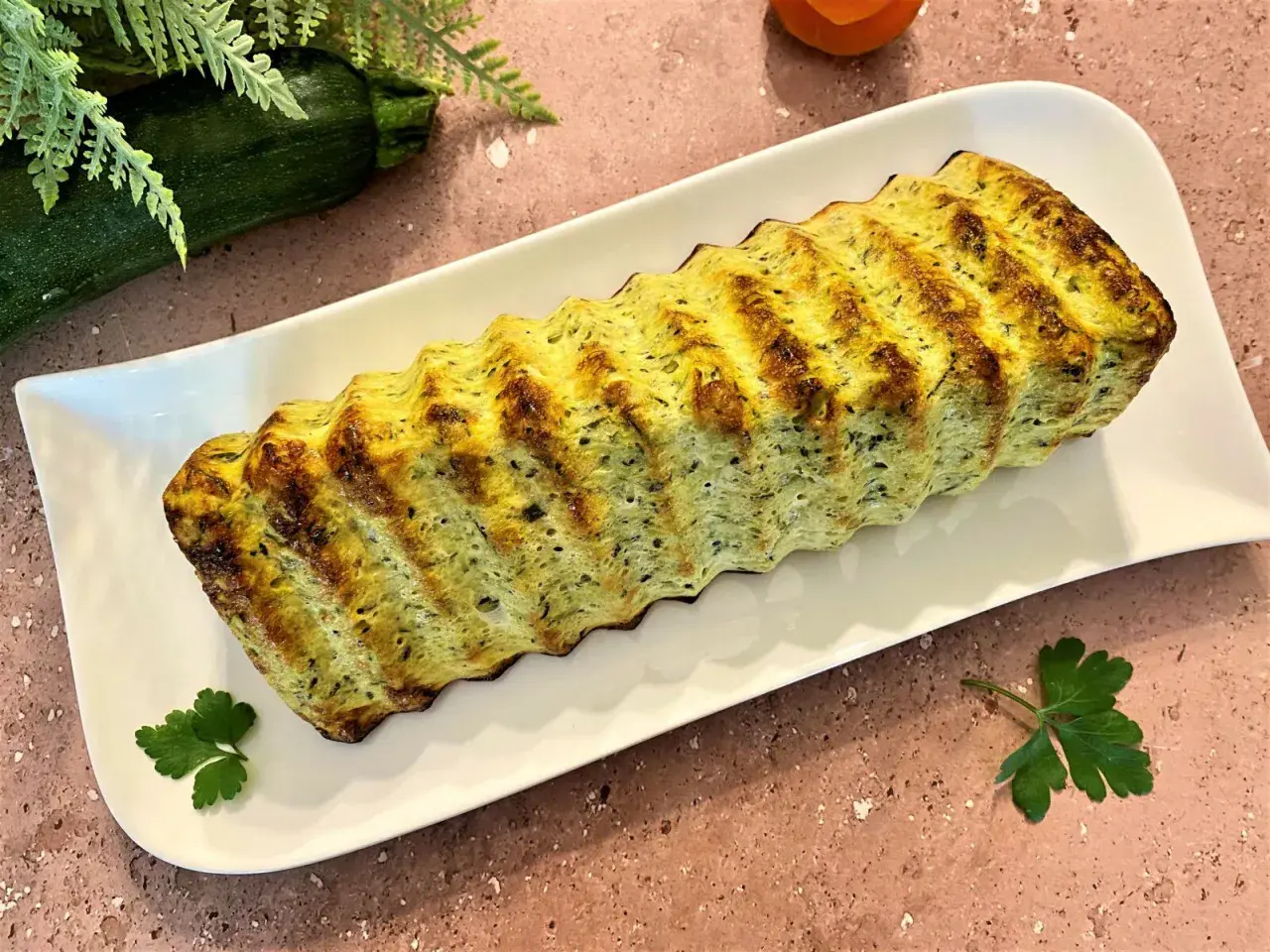 Un délicieux pain de courgettes, doré et savoureux, servi sur une assiette blanche. Parfait pour un repas léger.