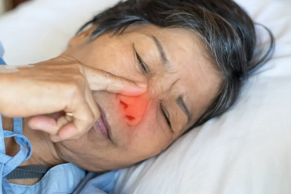 Una persona mayor con un dedo en la nariz, con una zona roja que indica dolor o irritación. ¿Qué pasa si te comes los mocos?
