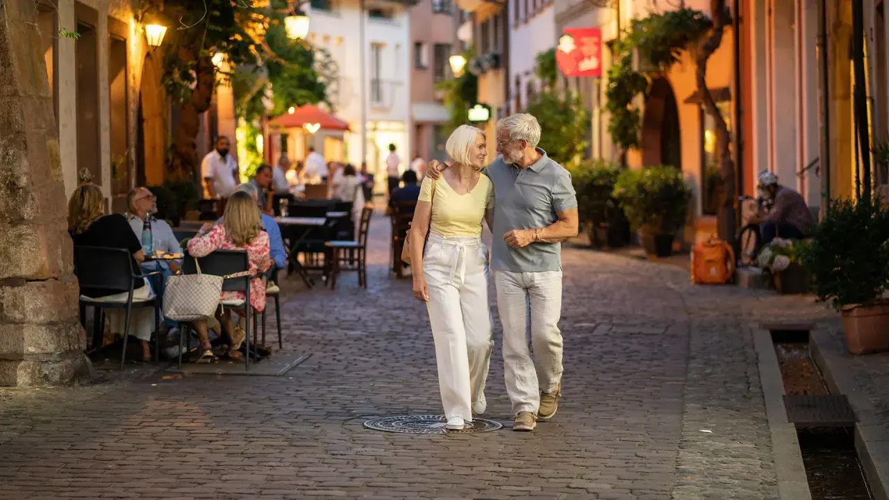 Ein älteres Paar spaziert abends durch eine Gasse in Freiburg. Was kann man in Freiburg machen? Hier: gemütlich essen gehen und die Atmosphäre genießen.