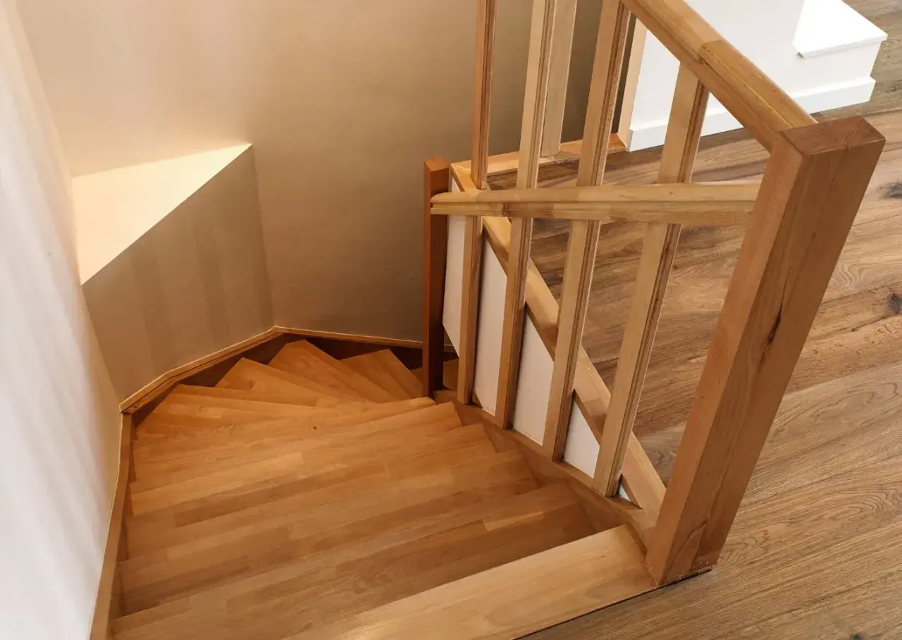 Holztreppe mit geschwungenen Stufen und einem hölzernen Geländer. Die Treppenstufen streichen das Licht und laden zum Hinaufgehen ein.