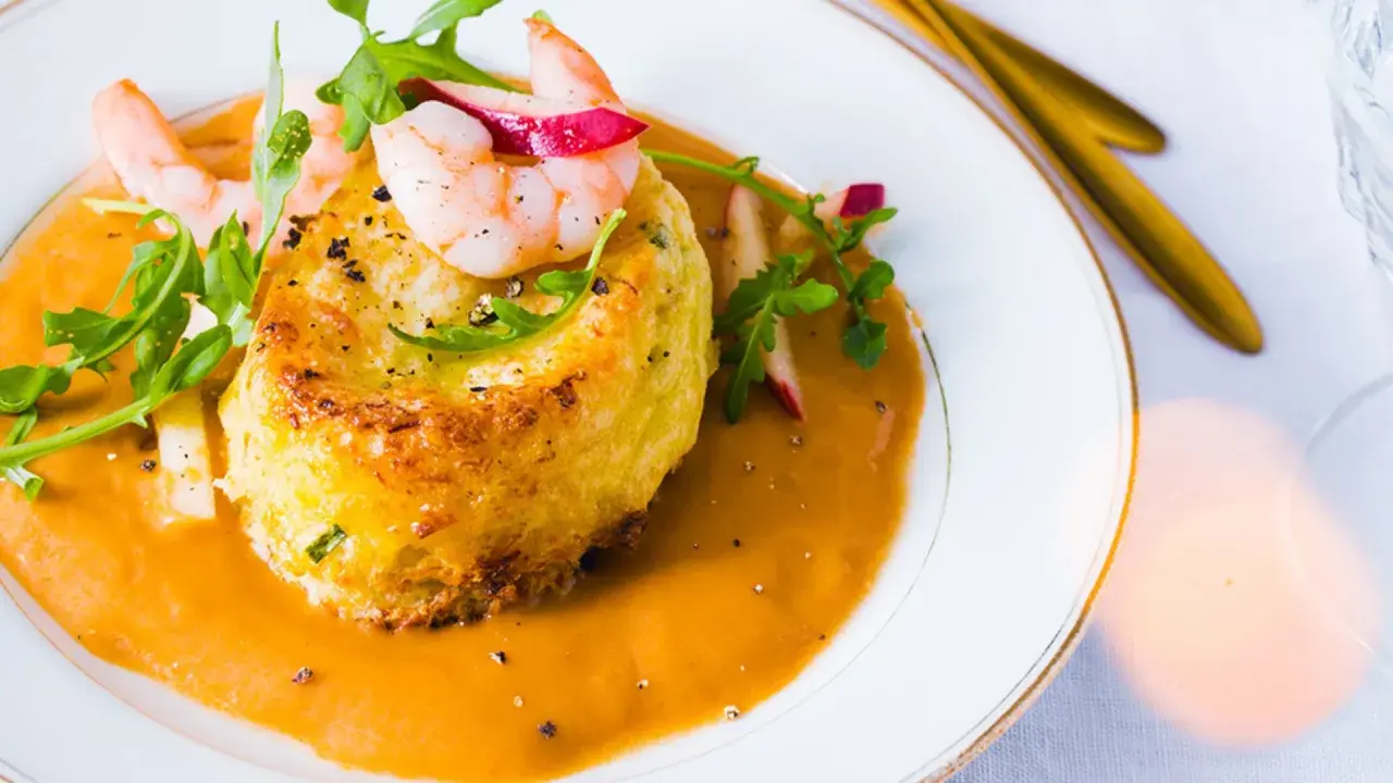 Un délicieux soufflé de crabe, nappé d'une bisque onctueuse et garni de crevettes et de roquette.