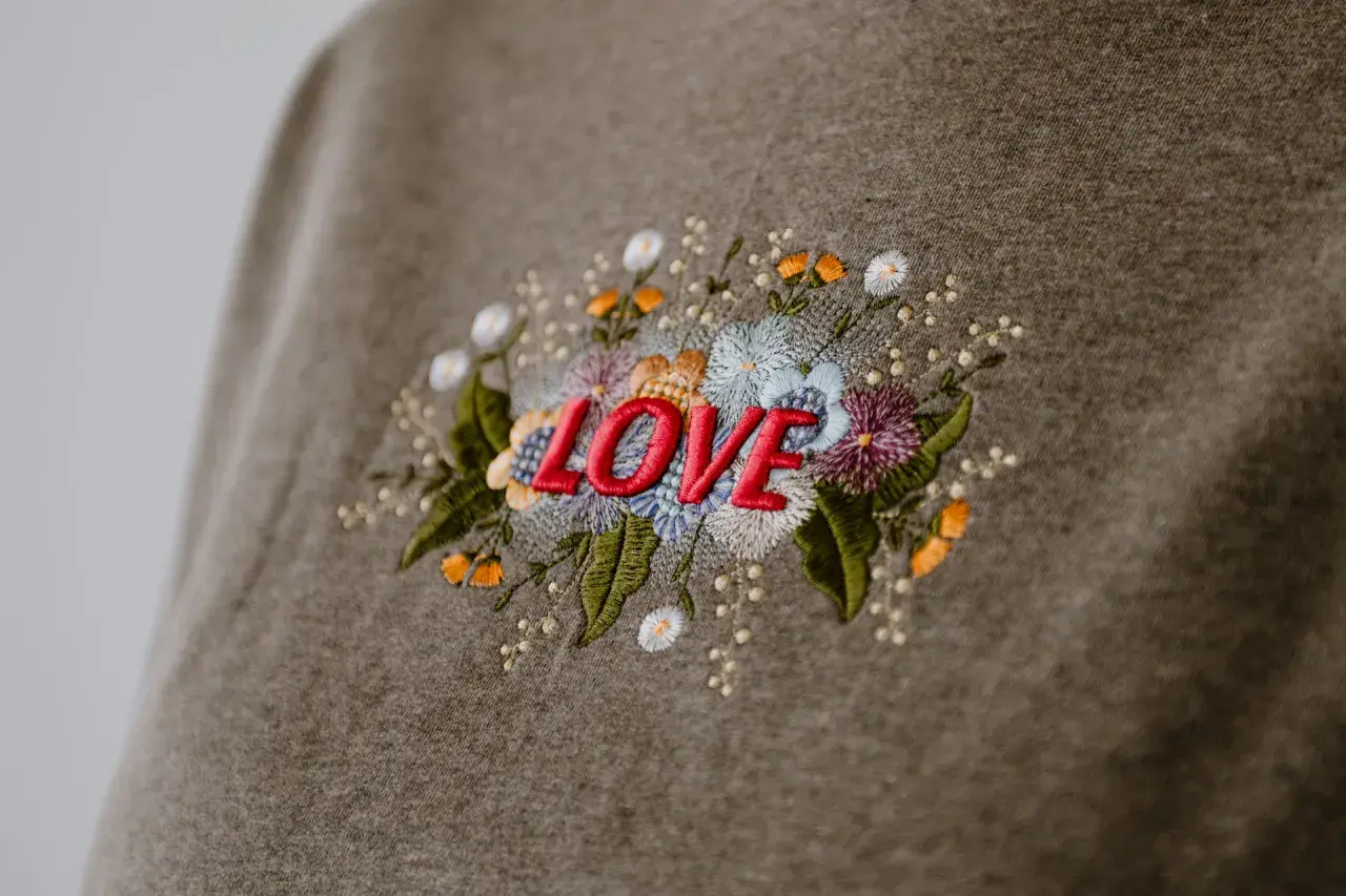 Besticktes Sweatshirt mit dem Wort "LOVE" umgeben von bunten Blumen. Zeigt, was man besticken kann.