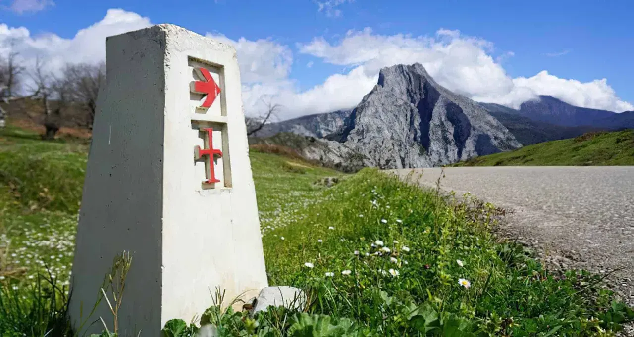Señal del camino lebaniego, indicando la ruta. El paisaje montañoso sugiere la dificultad del camino.