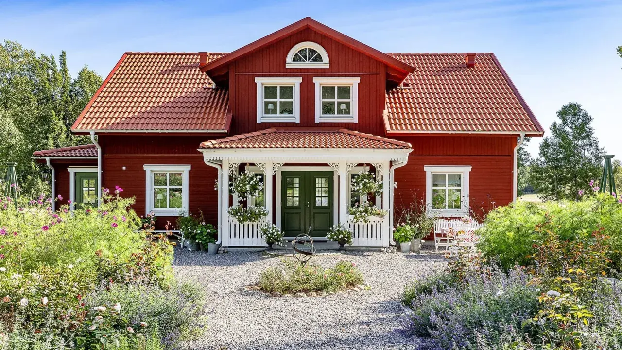 Vackert rött hus med vita detaljer, en veranda och en blomstrande trädgård. Ett perfekt exempel på att **bygga hus i gammal stil**.