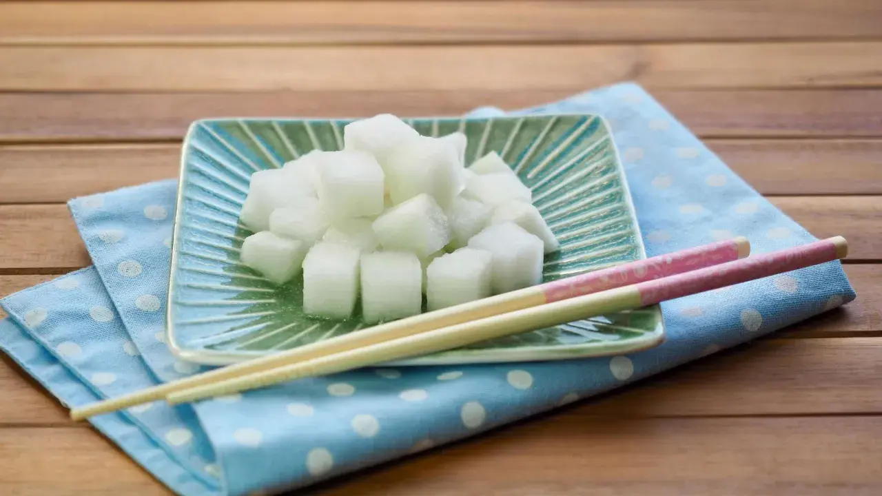 Würfel von daikon rettich auf einem grünen Teller, daneben Stäbchen auf einem blauen Tupftuch.