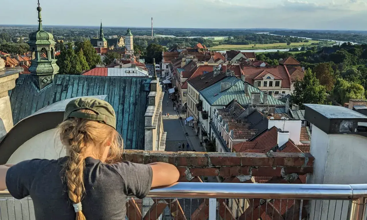 Widok z góry na Sandomierz, z dziewczynką w czapce na pierwszym planie. W oddali widać Wisłę i charakterystyczną Brama Opatowska.