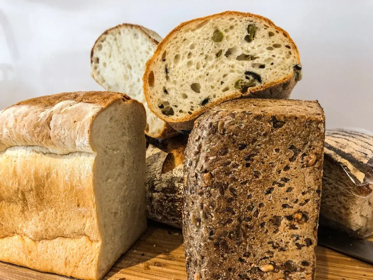 Różnorodne pieczywo, w tym bochenek z ziarnami i kromka z oliwkami. Czy chleb żytni ma gluten? Tak, większość chlebów, w tym żytni, zawiera gluten.