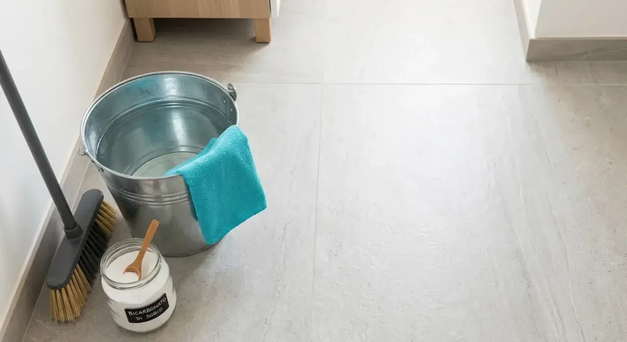 Secchio, scopa e barattolo di bicarbonato per pavimenti, pronti per una pulizia profonda.
