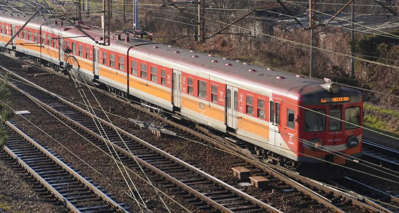 Czerwono-pomarańczowy pociąg elektryczny EN57 na torach.