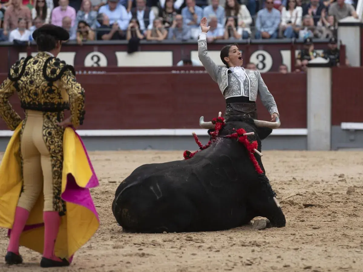 Una torera, entre los **recortadores de toros**, se enfrenta a un toro negro en la arena.