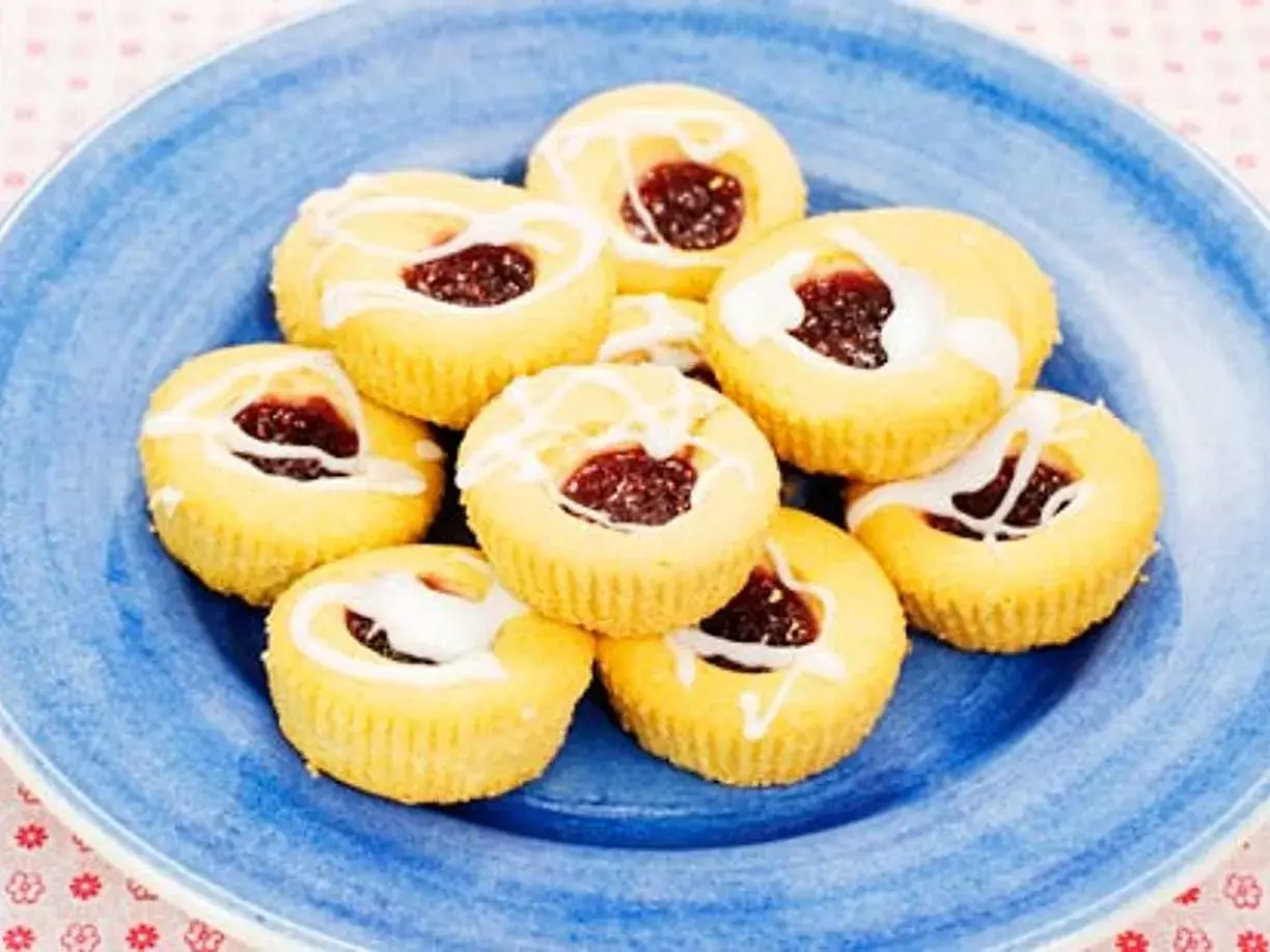 Hallongrottor recept: små, runda kakor med hallonsylt i mitten och glasyr på en blå tallrik.