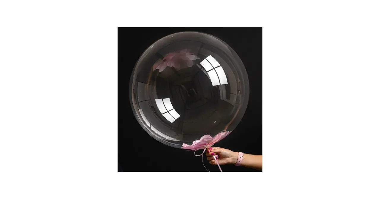 Przezroczysty bubble balon z różowymi płatkami kwiatów w środku i na dole, trzymany przez dłoń.