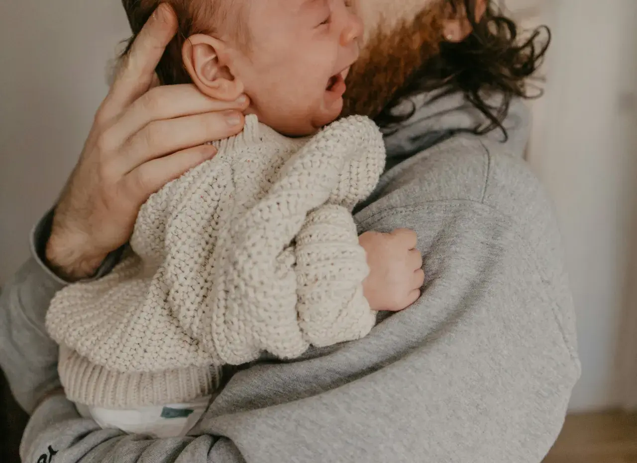 En pappa tröstar sitt ledsna barn som verkar ha bebis hård i magen.