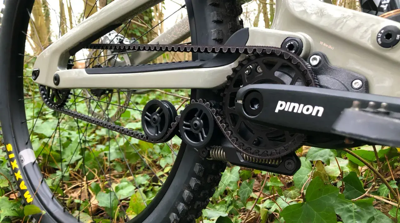 Close-up of a belt drive mountain bike's drivetrain, featuring a Pinion gearbox and Gates Carbon Drive belt, ready for off-road adventures.