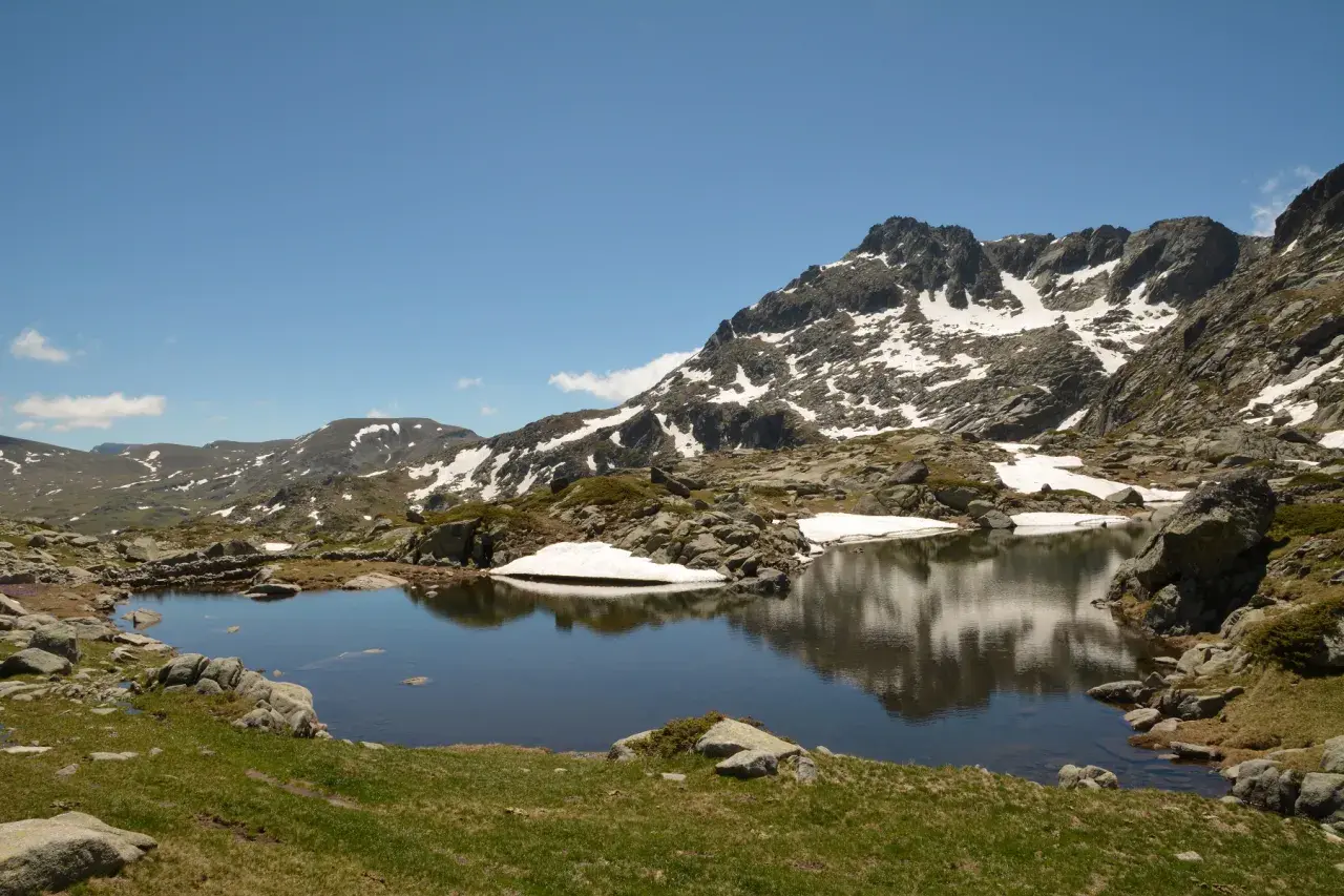 Góry Pirin z jeziorem odbijającym skaliste szczyty i resztki śniegu.