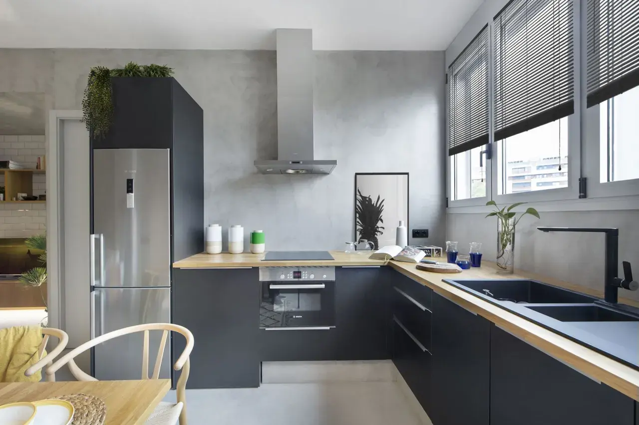 Cocina moderna con paredes de microcemento, muebles oscuros, encimera de madera y electrodomésticos de acero inoxidable.
