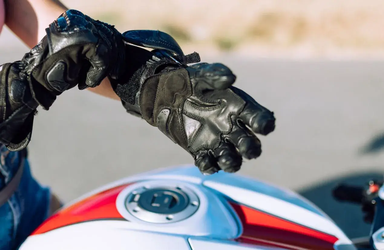 Persona se ajusta guantes de moto negros. Es obligatorio llevar guantes en moto para protegerse.