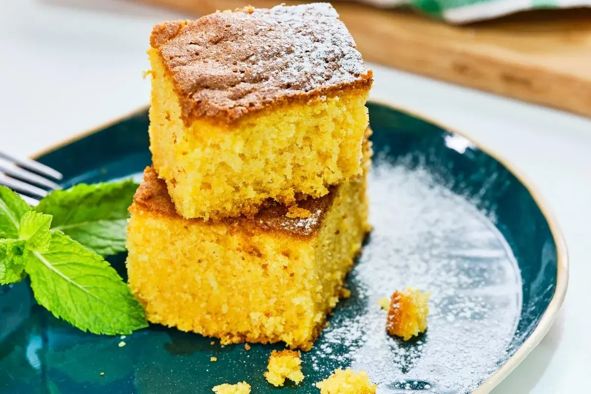 Dos porciones de bizcocho de calabaza apiladas, espolvoreadas con azúcar glas, junto a hojas de menta fresca en un plato azul.