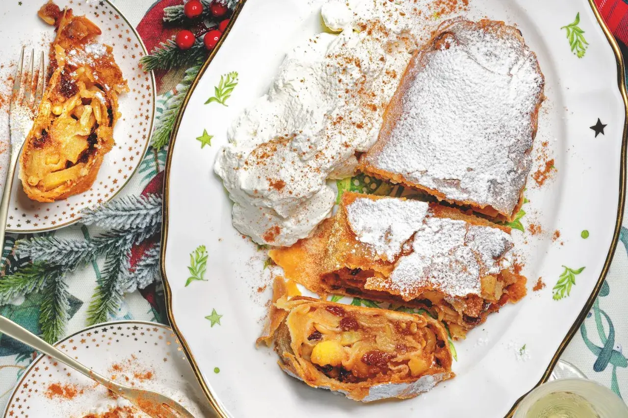 Delizioso strudel di mele con pasta sfoglia, cosparso di zucchero a velo e servito con panna montata e cannella.
