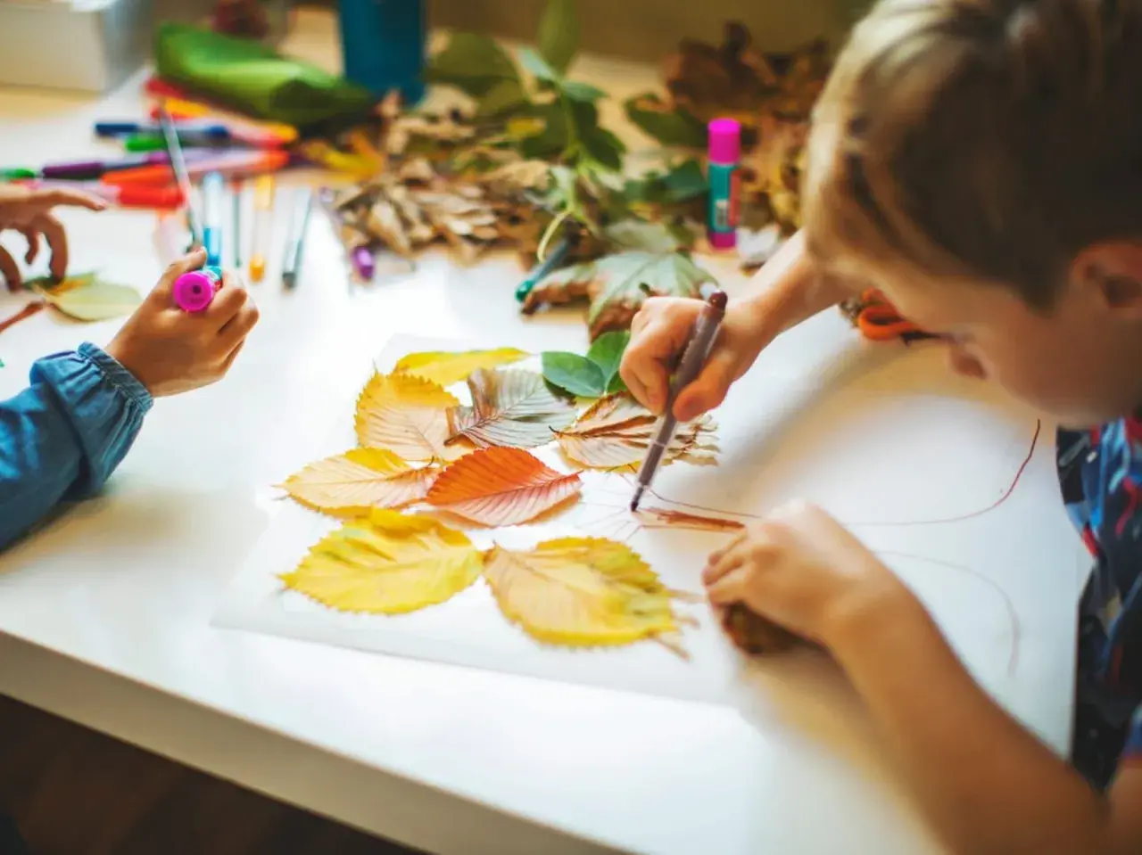 Niños creando arte con hojas de otoño. Actividades para trabajar las plantas en infantil, usando rotuladores y hojas secas para dibujar.