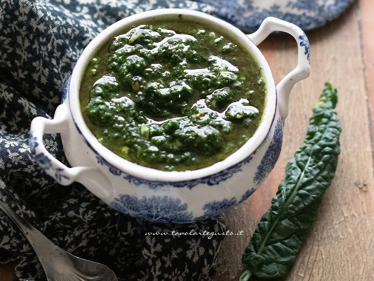 Pesto di cavolo nero in una ciotola decorata, accanto a una foglia fresca. Un condimento sano e saporito.