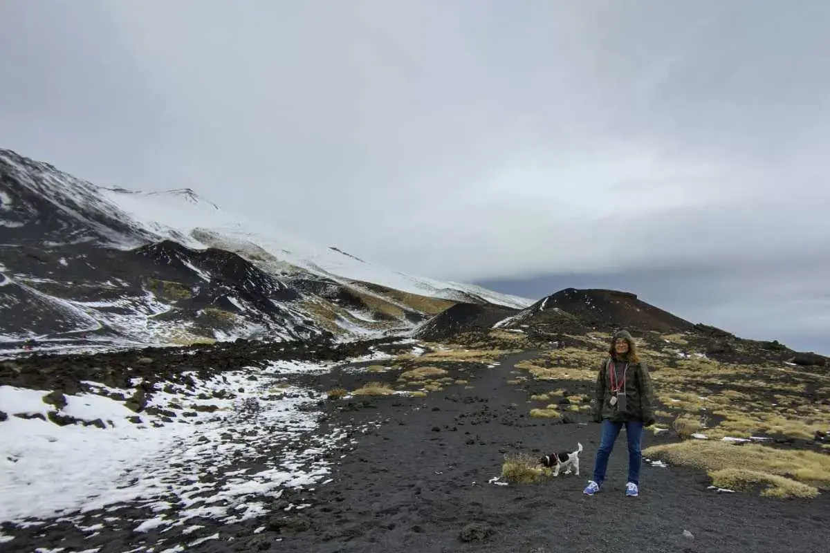 Una donna e il suo cane esplorano il paesaggio lunare dell'Etna in Sicilia, con neve e rocce vulcaniche.