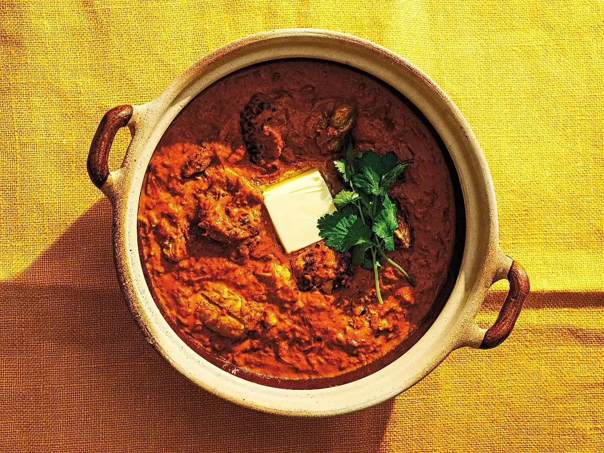 En skål med krämig chicken tikka masala, toppad med en smörbit och färsk koriander. Perfekt för en mysig middag.