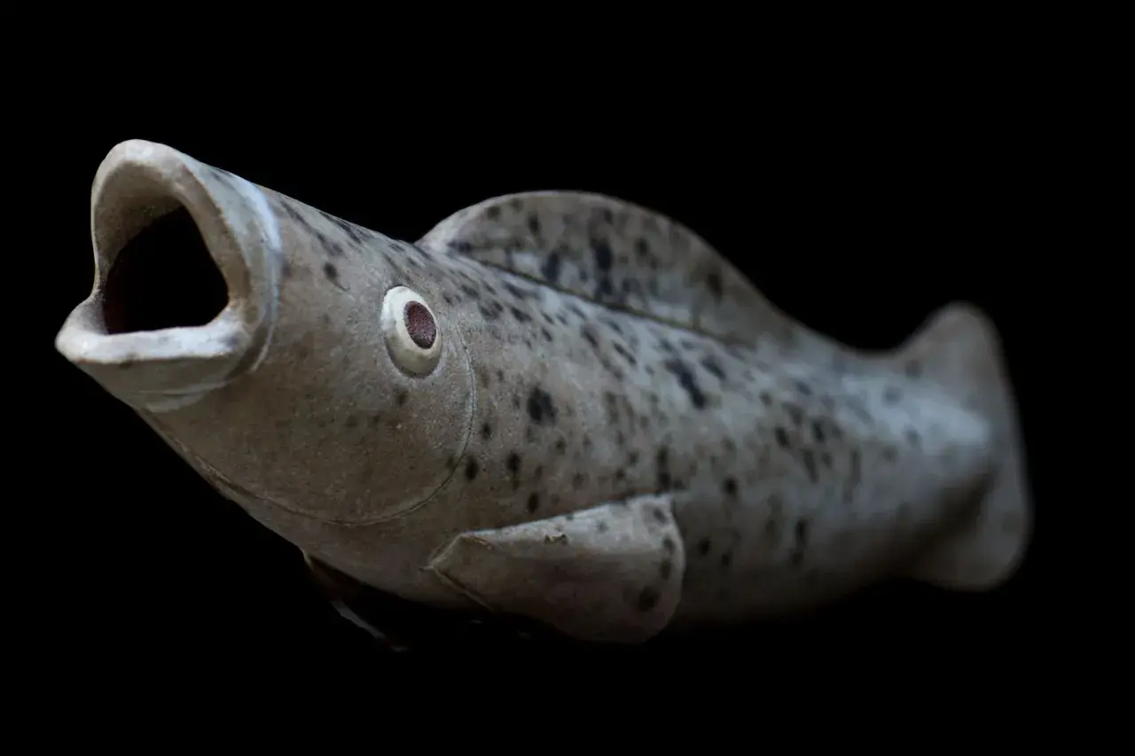Pesce in ceramica con bocca aperta, occhio sporgente e macchie scure, un'opera che ricorda lo stile di Tonino Negri.