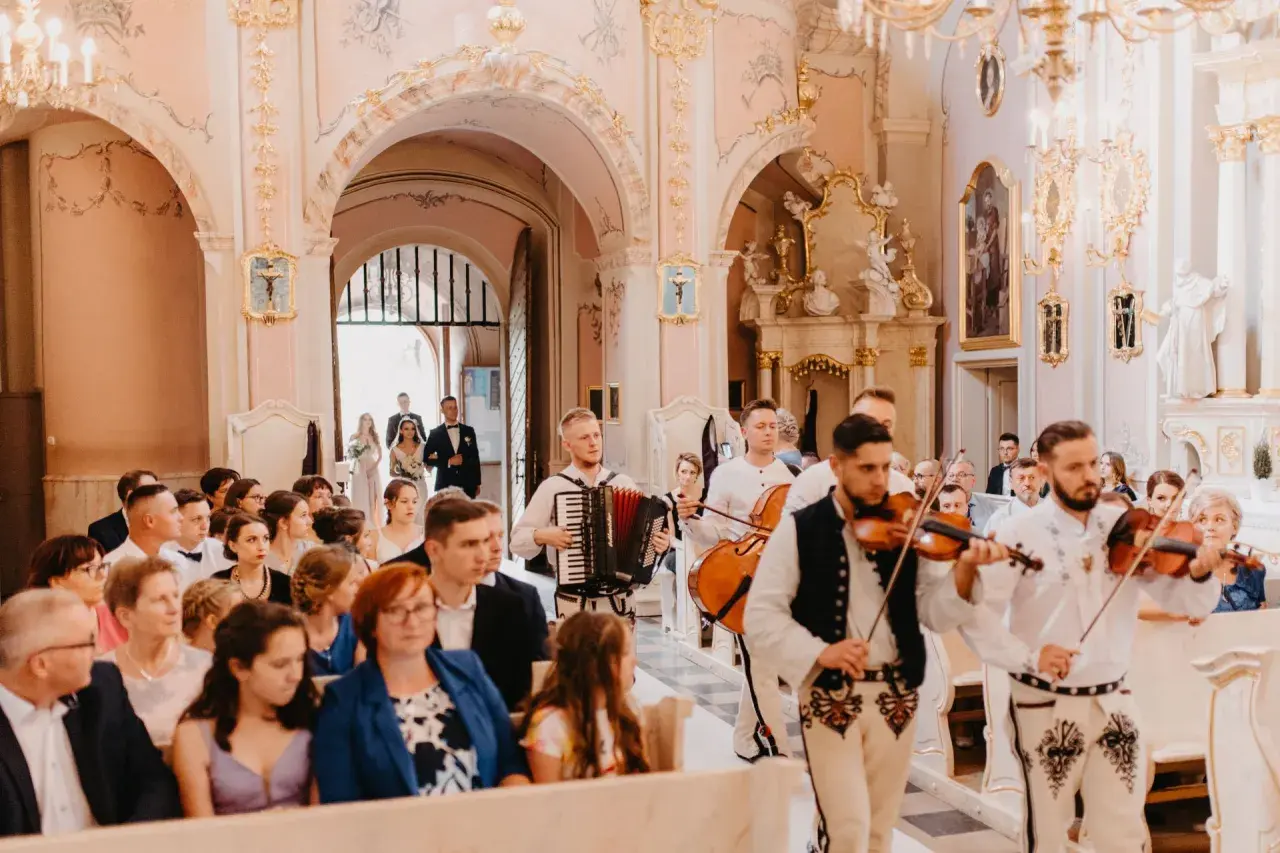 Muzycy grają pieśń na wejście w kościele. W tle para młoda wchodzi do świątyni.