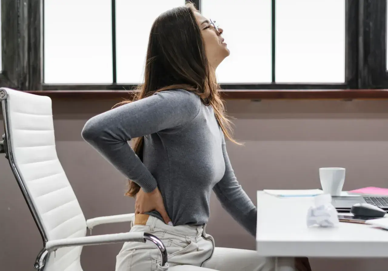 Femme souffrant de mal de dos, possiblement une hernie discale, à cause du travail assis.