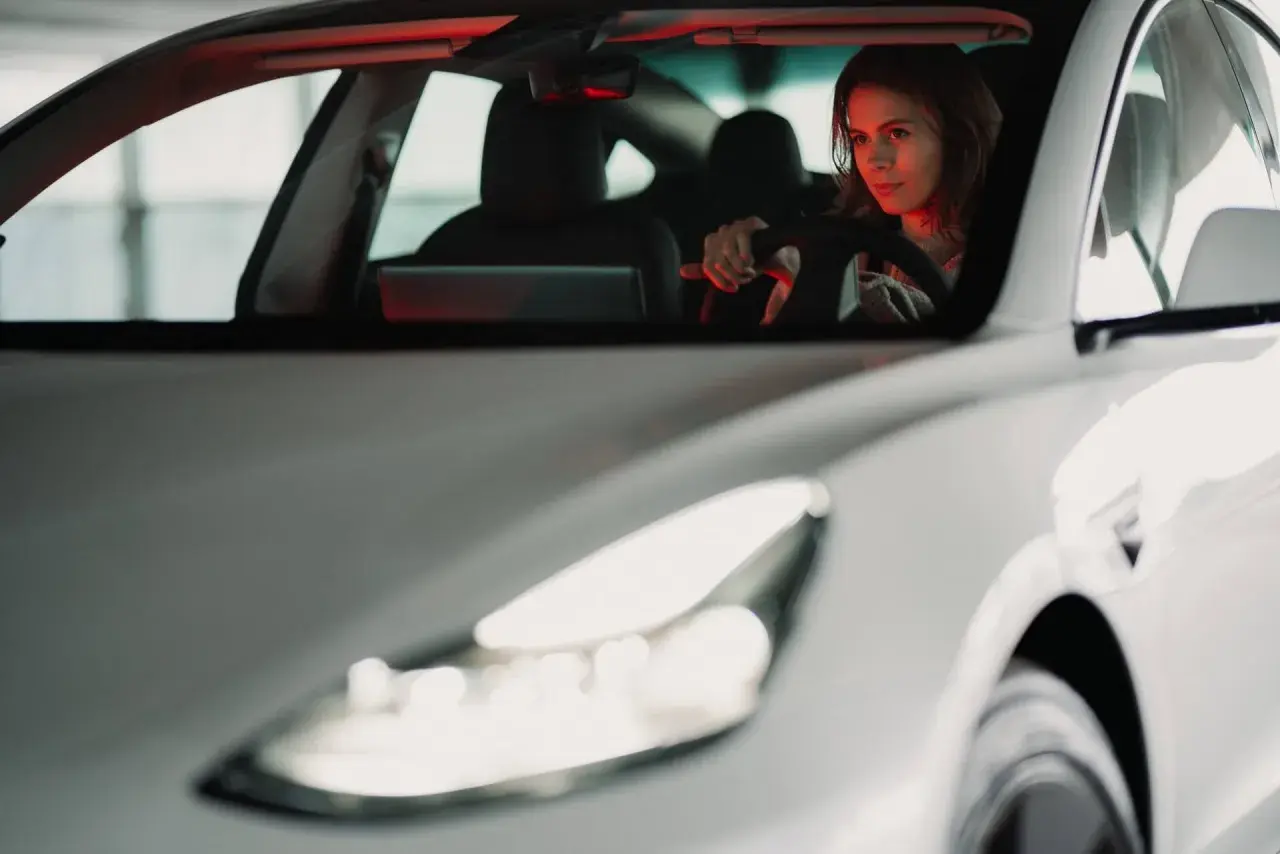 Kobieta za kierownicą białego samochodu. Zastanawia się, leasing co to? Może to sposób na nowy pojazd?