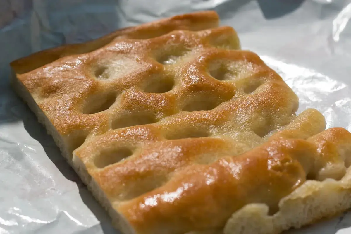 Focaccia genovese, un must per capire cosa mangiare a Genova. Dorata, soffice e profumata, perfetta da gustare in ogni momento.