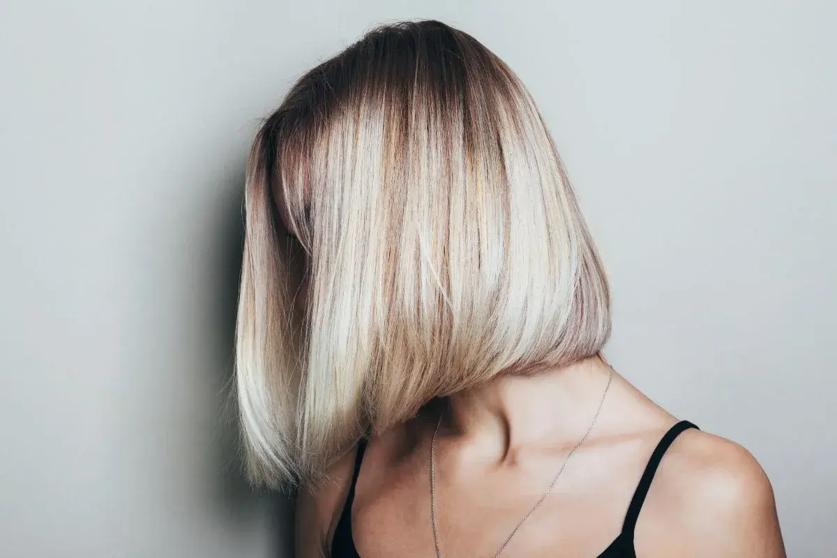 Kobieta z asymetryczną, blond fryzurą typu bob, z ciemniejszymi odrostami.