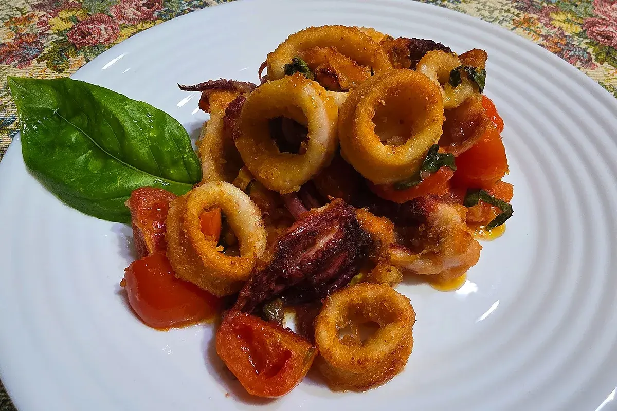 Anelli di calamari croccanti e pomodorini cotti nella friggitrice ad aria, guarniti con una foglia di basilico.