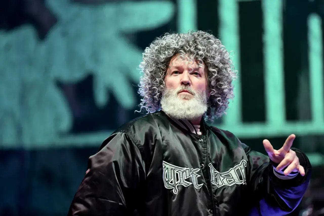 Fred Durst z Limp Bizkit na koncercie, z charakterystyczną fryzurą i brodą, w czarnej kurtce z logo zespołu.