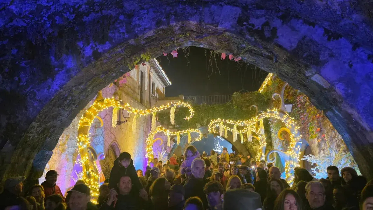 Gente disfrutando del mercado navideño en Cartes, con luces brillantes y ambiente festivo bajo un arco de piedra.